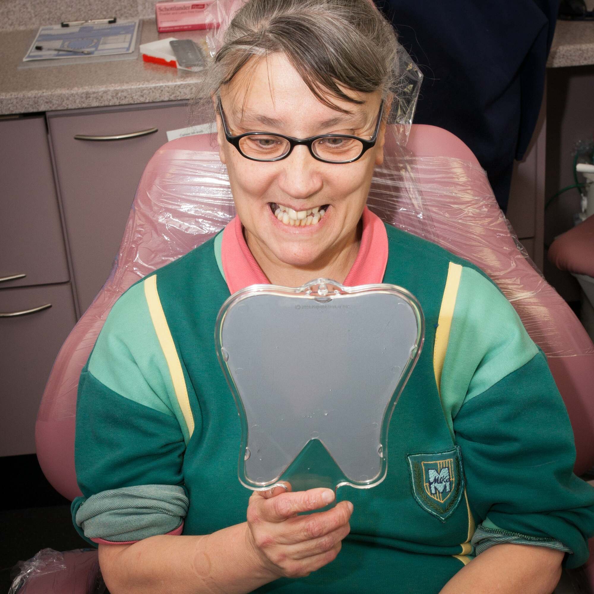 A person in a dental chair, looking at their teeth in a mirror.