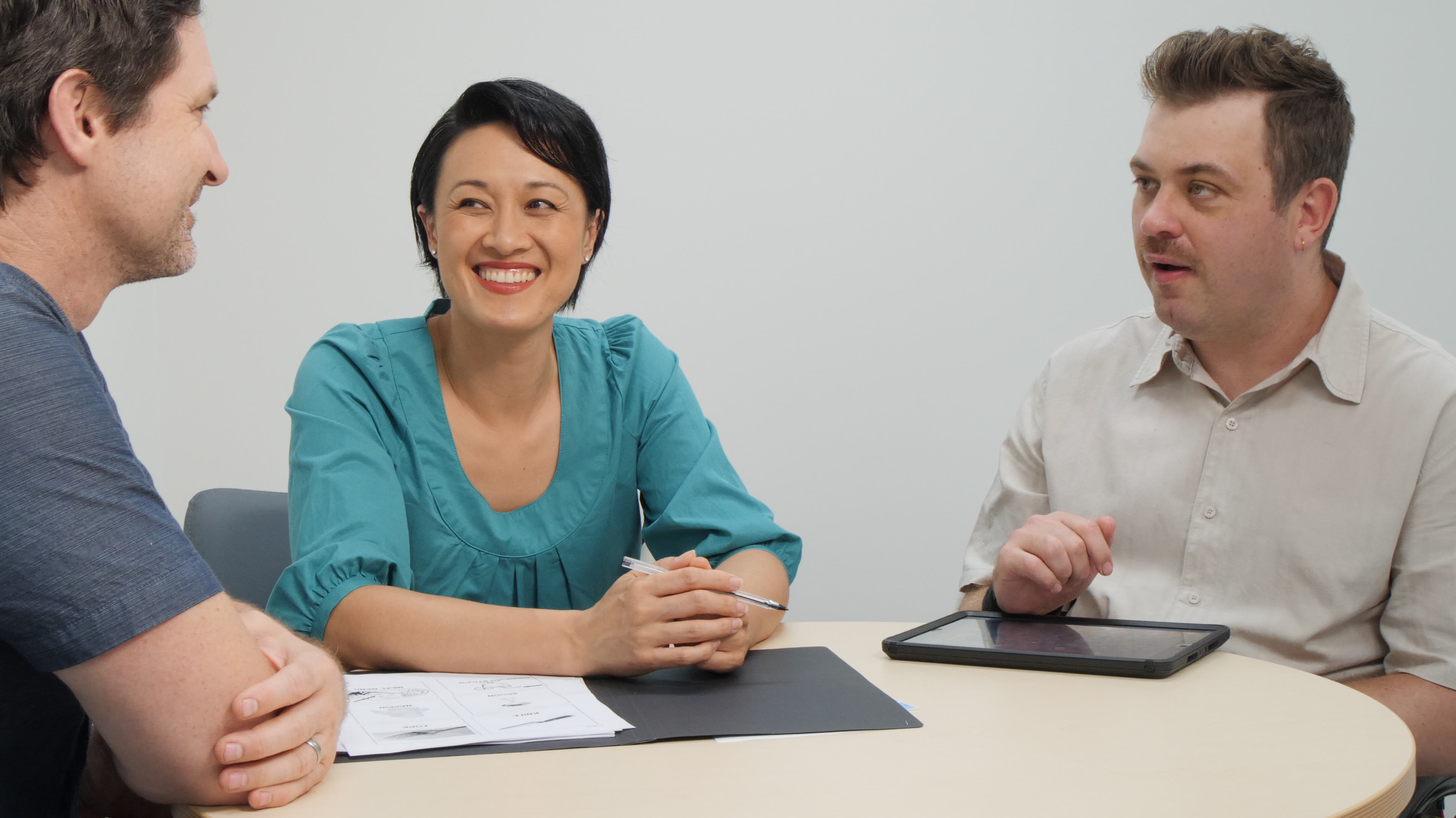 Three people sit around a table having a conversation.