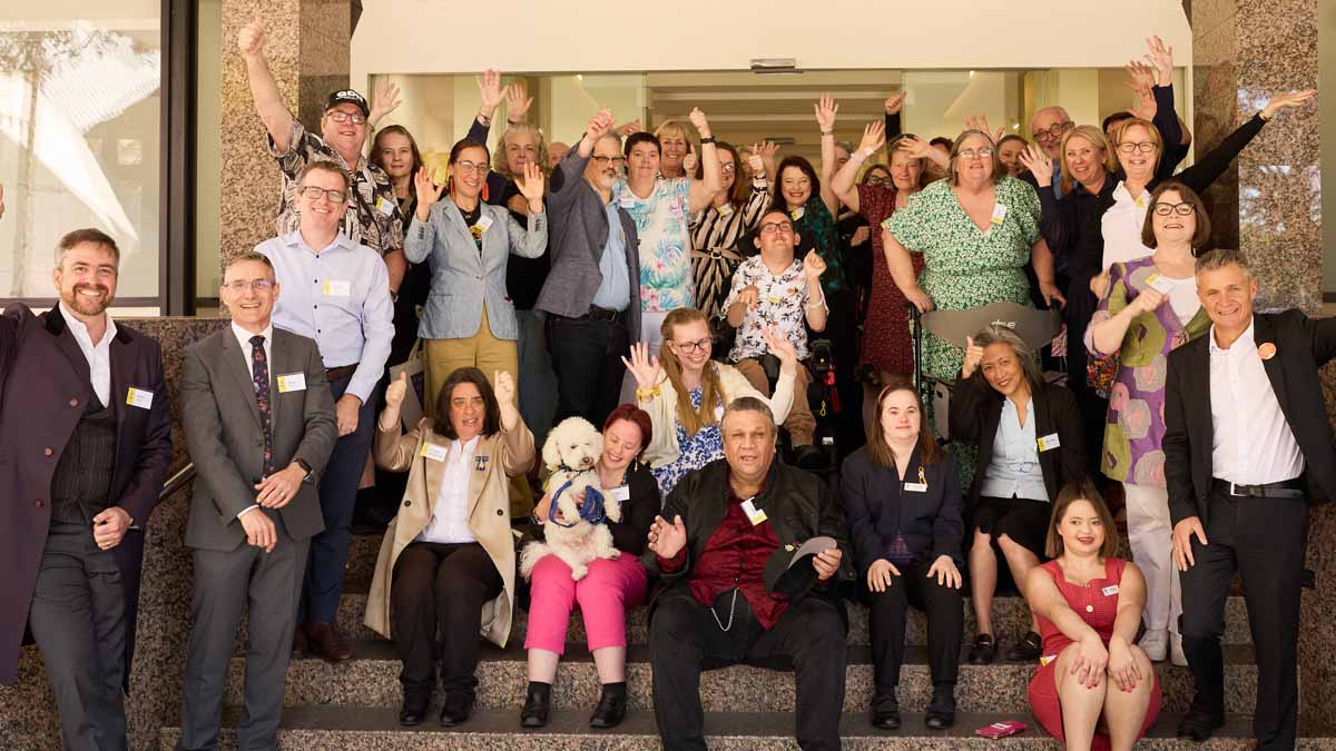 A group of 26 people who work at the Centre. They are smiling and waving.
