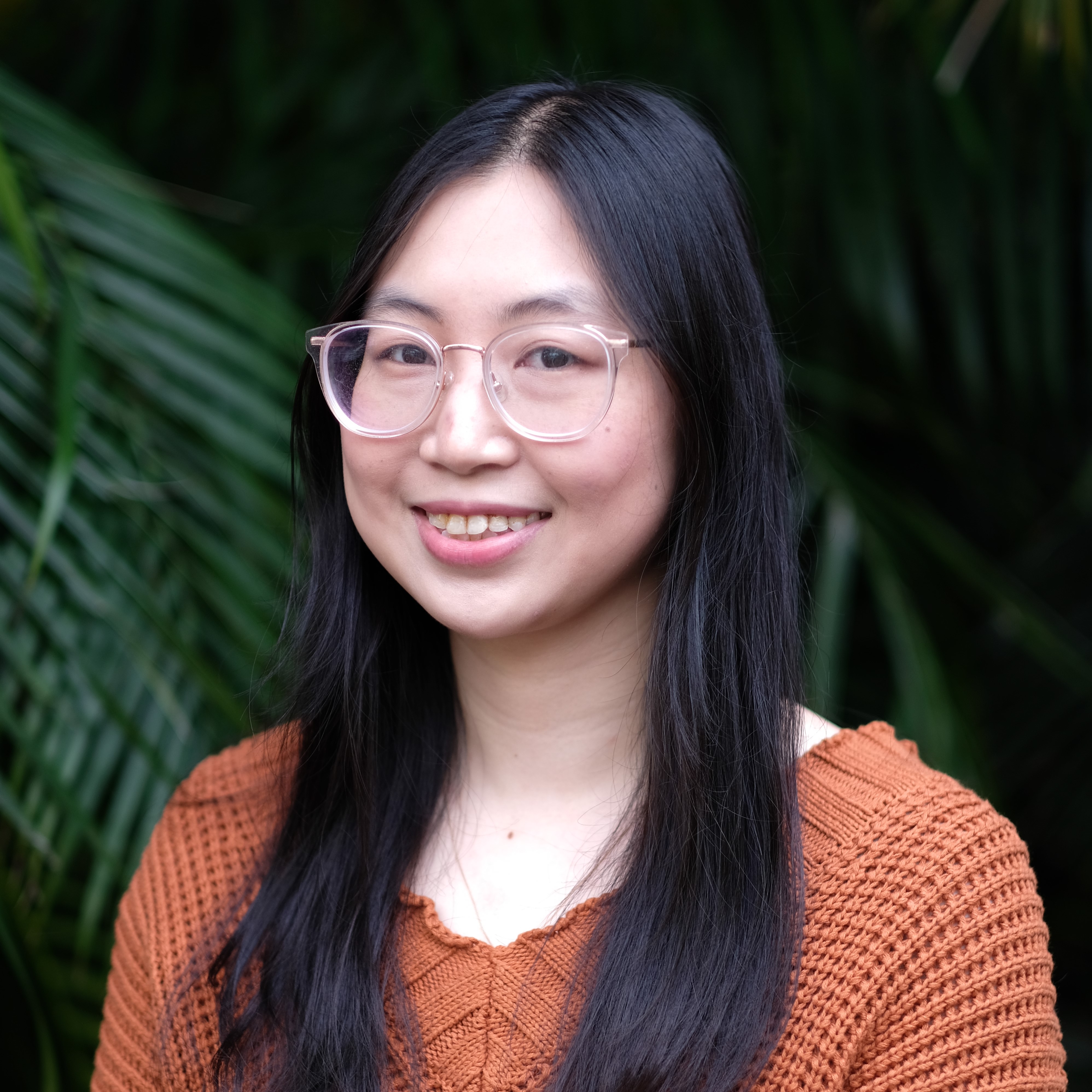 A photo of Jenna Zhao. The photo is of Jenna's shoulders and head. She is wearing glasses and smiling at the camera.