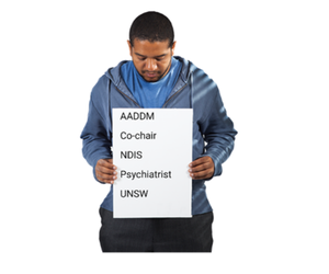 Photo of a man holding a list of words. The words are AADDM, Co-chair, NDIS, Psychiatrist and USNSW.