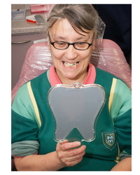 Photo of a woman in a dental chair looking at her teeth in a hand-held mirror.