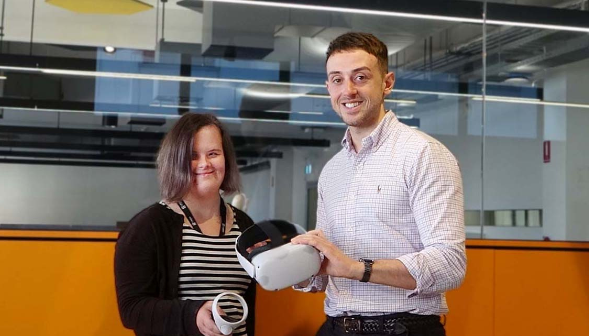 A photo of two researchers. One has intellectual disability. They are both holding parts of a virtual reality headset.