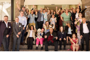 Photo of a big group of people who work at the Centre smiling and waving at the camera.