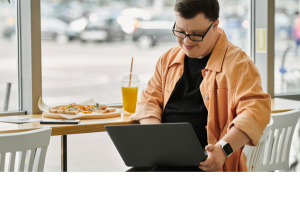 A man with intellectual disability sitting in a cafe and typing on a laptop.