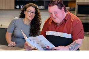 Photo of a woman and a man with intellectual disability sitting together. The man is reading an Easy Read document about research.