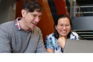 Photo of two people looking at a computer and smiling.