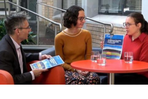 Photo of three people sitting around a table holding a framework document.