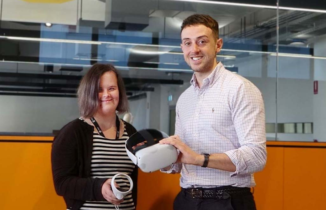 Photo of two researchers. One has intellectual disability. They are holding parts of a virtual reality headset.