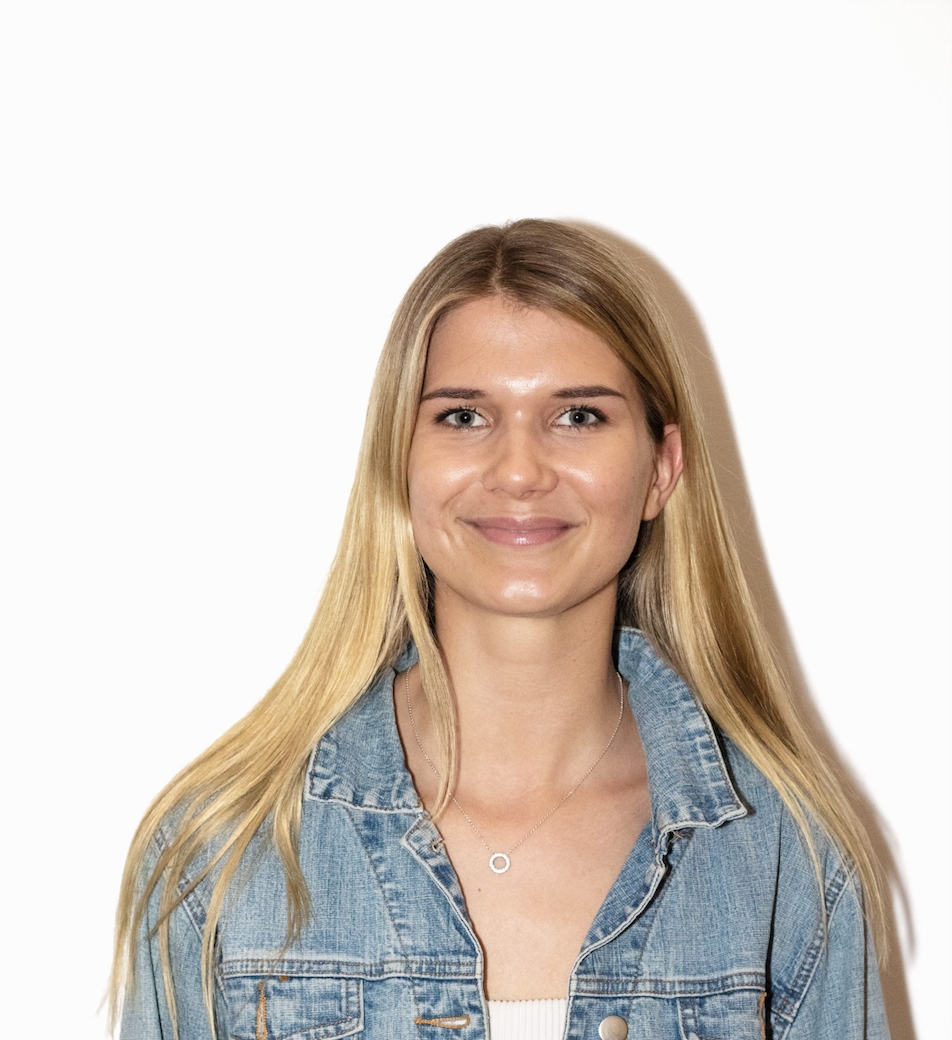 A photo of Charlotte Bridge. She is wearing a denim jacket. She has long blonde hair. She is smiling at the camera.