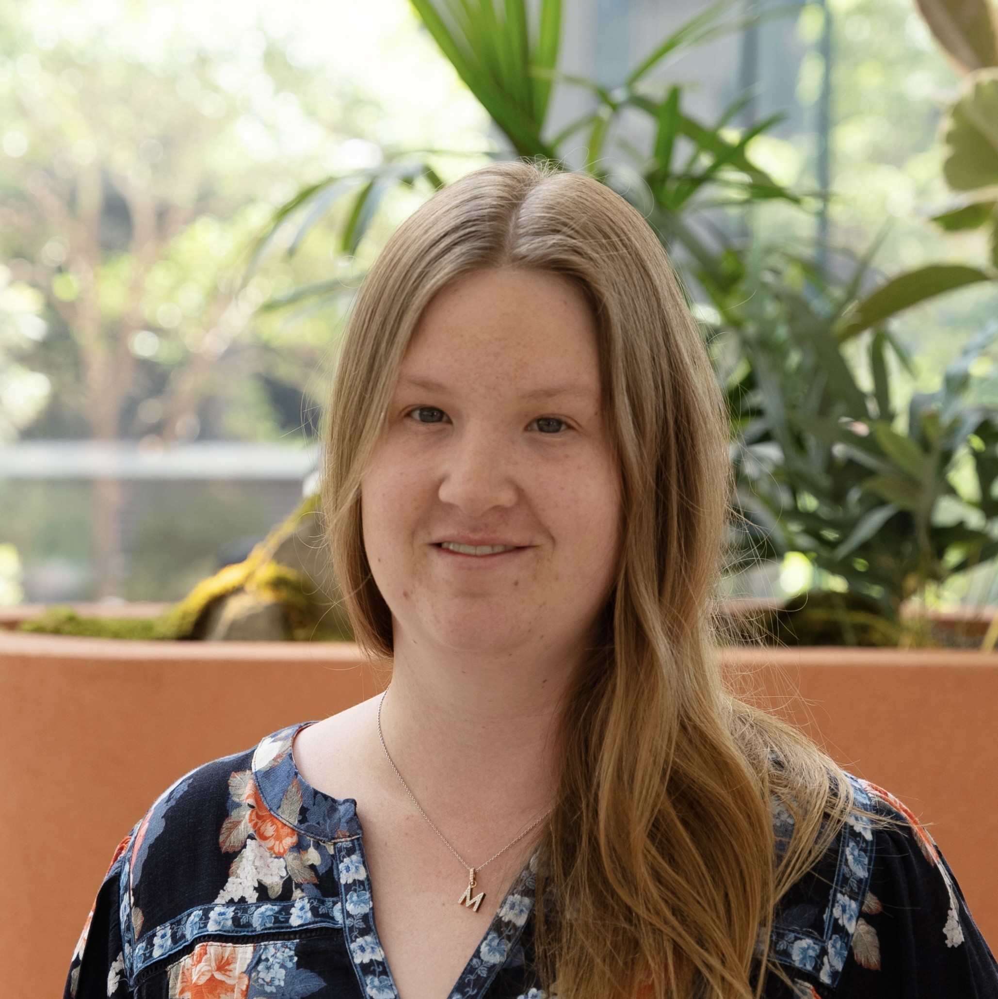 Photo of Madison Booth. She is sitting in front of a green plant and smiling at the camera.