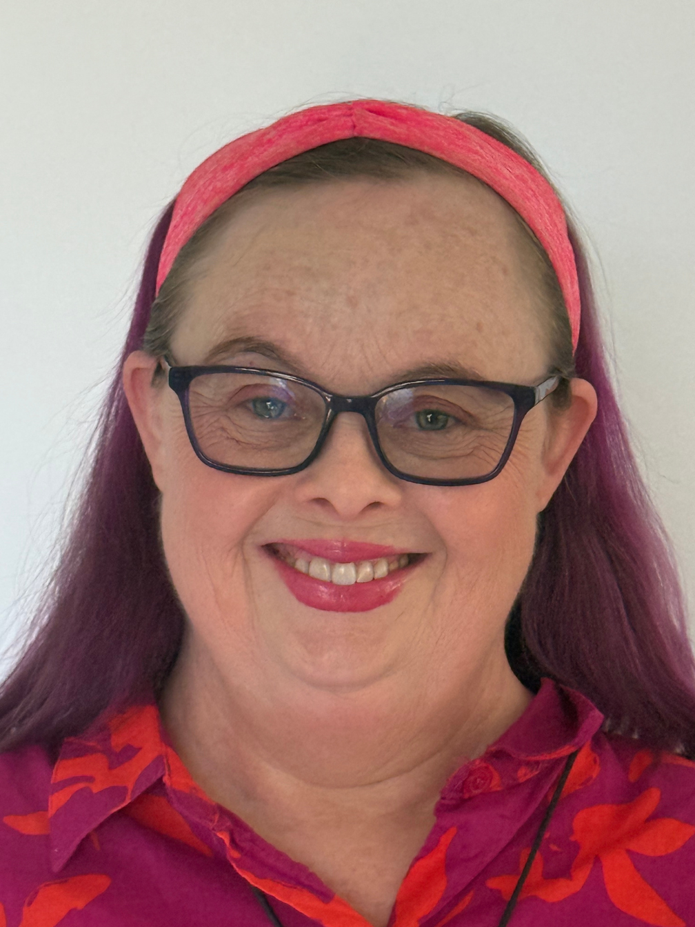 A photo of Natasha Tomlinson. She is wearing a purple and orange shirt and smiling at the camera.