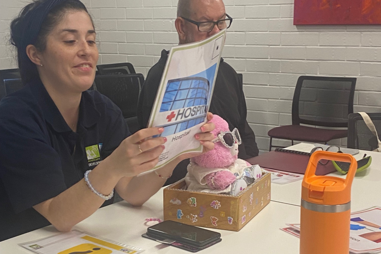 Photo of two people sitting at a table. One is looking at a booklet.
