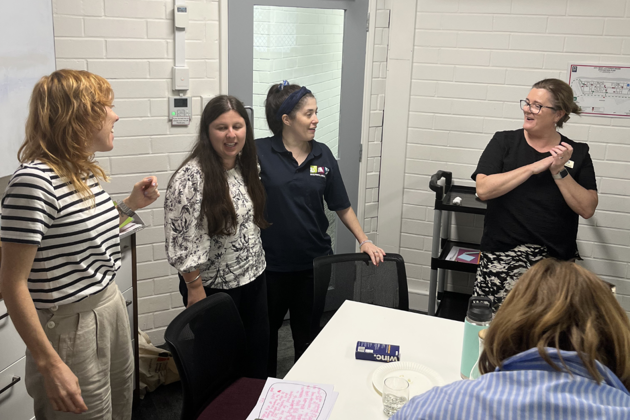 Photo of some people standing in a room. They are talking together.