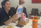 Photo of two people sitting at a table. One is looking at a booklet.