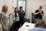 Photo of some people standing in a room. They are talking together.