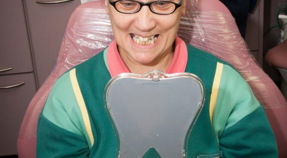 A person in a dental chair, looking at their teeth in a mirror.