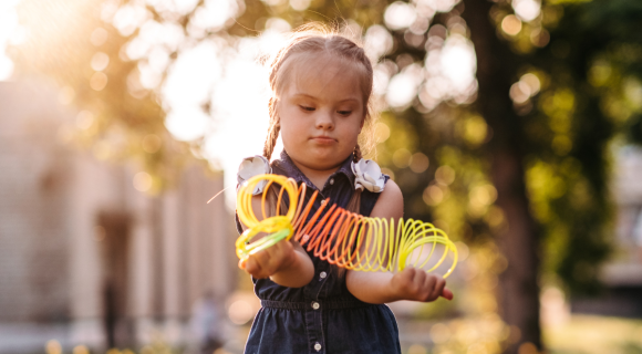 Photo of a young girl with intellectual disability outside playing with a slinky.