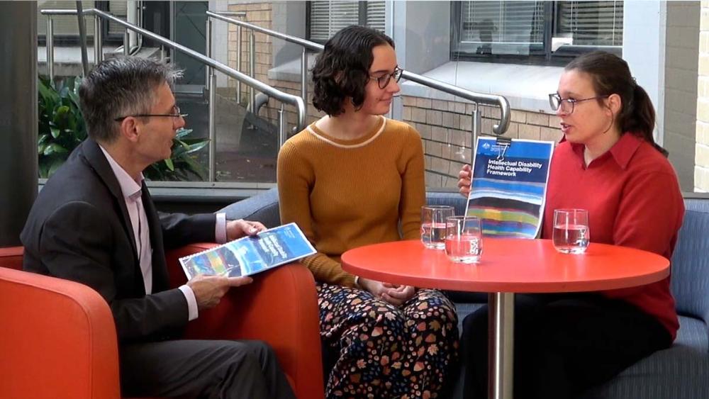 Tahli, Emily and Julian sitting at a cafe table talking about the framework. 