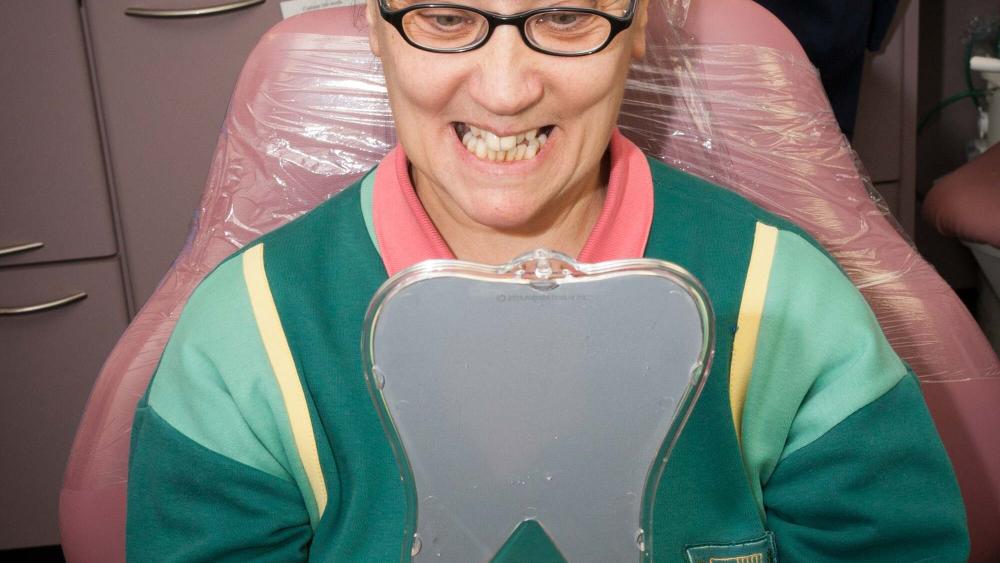 A person in a dental chair, looking at their teeth in a mirror.