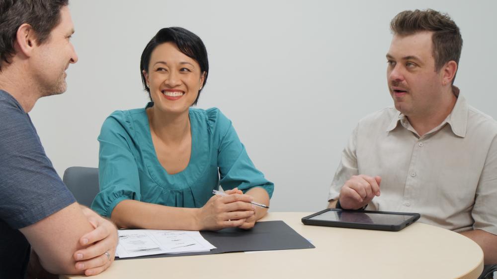 Three people sit around a table having a conversation.
