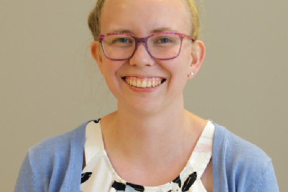 Profile photo of Katie Brooker. She is wearing glasses and smiling. She has a pale blue cardigan on.