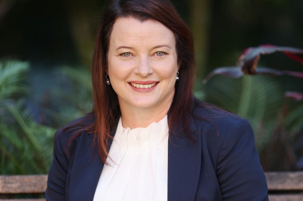 A photo of Cathy Franklin. She has long brown hair. She is wearing a navy blue blazer and a white blouse. She is smiling at the camera.