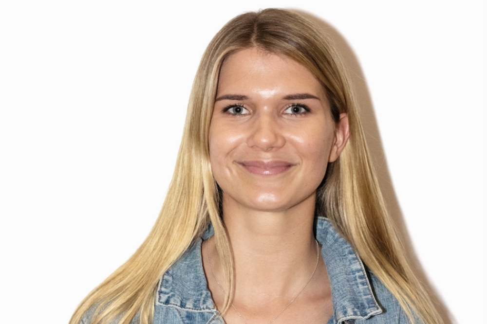 A photo of Charlotte Bridge. She is wearing a denim jacket. She has long blonde hair. She is smiling at the camera.