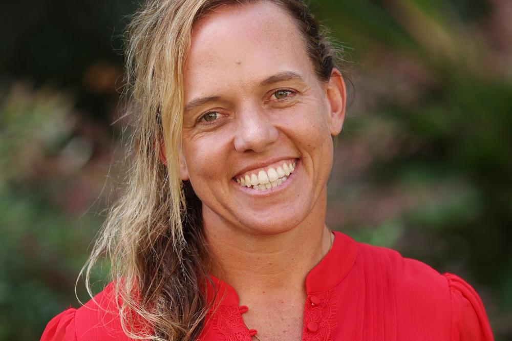 A photo of Kitty-Rose Foley. She is wearing a red shirt and smiling at the camera. She is standing outside.