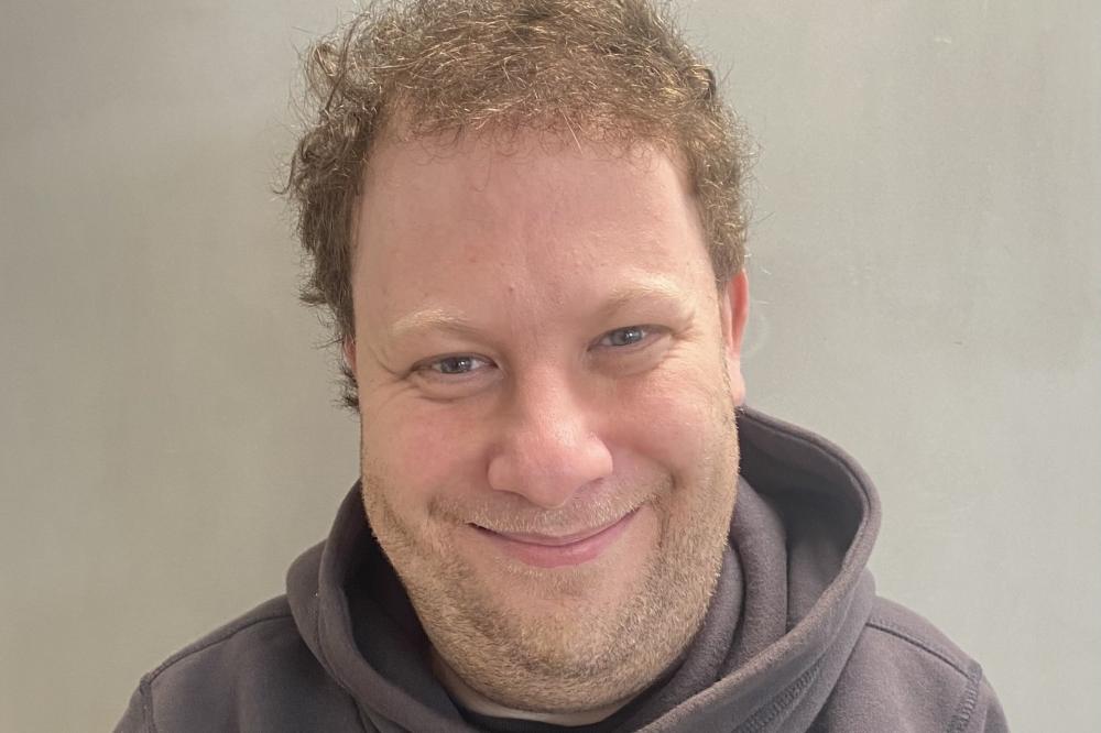 Photo of Michael Sarif. He is wearing a grey top and smiling at the camera.