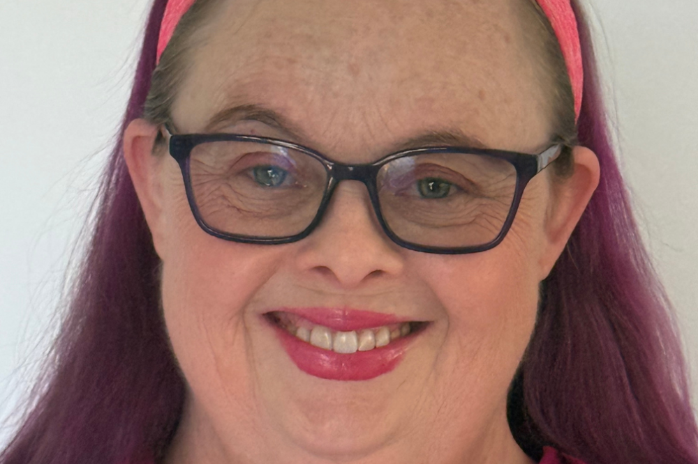 A photo of Natasha Tomlinson. She is wearing a purple and orange shirt and smiling at the camera.