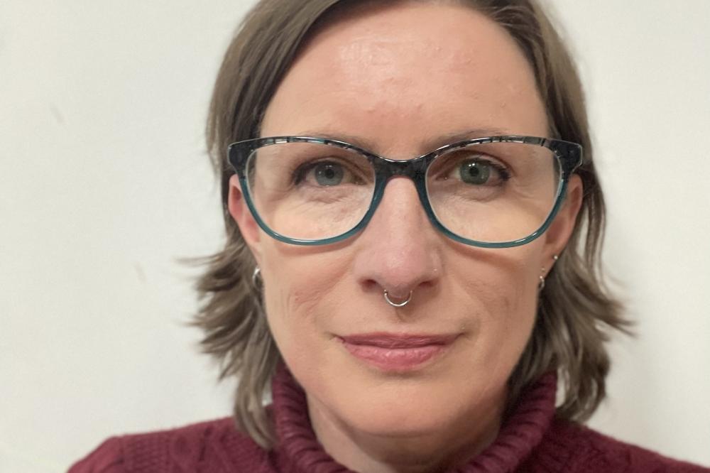 Photo of Danielle Carey. She is wearing a maroon top and glasses. She is smiling at the camera.