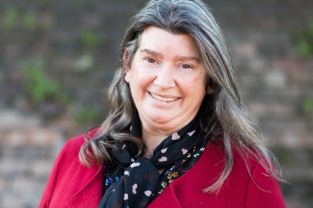 Photo of Raylene Griffiths. She is wearing a red top and smiling at the camera.